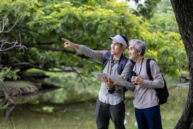 Asya 'lı son sınıf öğrencisi ve oğlu hafta sonu tatili macerası ve aile aktiviteleri için haritaya bakarken ormanda geziniyorlar.