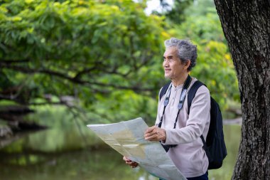 Asyalı son sınıf öğrencisi hafta sonu tatili macerası ve açık hava aktiviteleri için haritaya bakarken ormanın içinde geziniyor.
