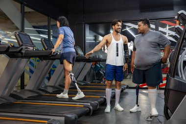 Ampütasyondan dolayı protez bacağı olan aşırı kilolu bir adama spor salonunda yürüyüş egzersizi yaparak sağlık ve sakatlık tedavisi için koşu bandı kullanıyor.