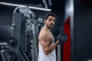 Beyaz sakallı, kaslı sporcu, spor yapmak ve egzersiz yapmak için arka planı koyu renk olan spor salonundaki kol ve kol kasları için çift halterli ağırlık antrenmanı yapıyor.