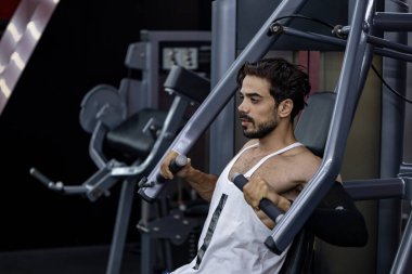 Kas geliştirme ve ağırlık kaldırma pratiği için spor salonunda göğüs pres makinesi üzerinde güçlü ve kaslı vücut eğitimi almış beyaz sakallı bir adam.