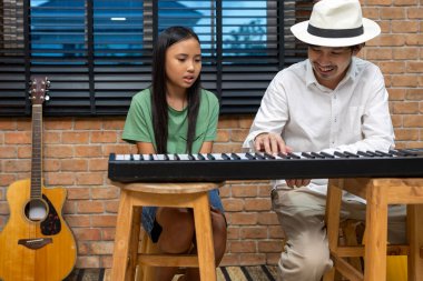 Genç Asyalı kız, okul sonrası müzik dersinde öğretmeninden klavye çalmayı öğreniyor. Çocukların yeteneği ve yeteneği gelişiyor.