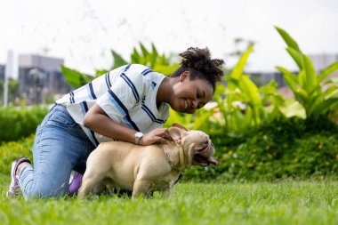 Afrika kökenli Amerikalı bir kadın yaz aylarında sabah egzersizi yaptıktan sonra çimlerin üzerindeki köpek parkında yürürken Fransız buldog yavrusuyla oynuyor.