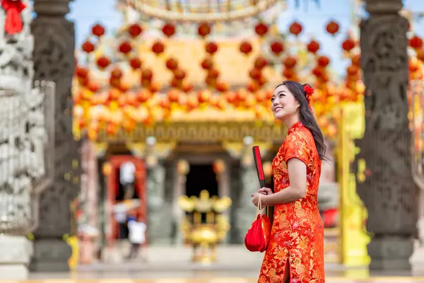 Kırmızı Cheongsam Qipao elbisesi giymiş Asyalı bir kadın elinde kağıt yelpaze tutarak Çin Budist tapınağını ziyaret ederken geleneksel kültür için yeni yıl boyunca