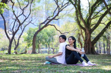 Genç Asyalı çift, sağlıklı yaşam ve aşk konsepti için halk parkında yoga minderinde otururken mutlu bir flört egzersizi yapıyor.