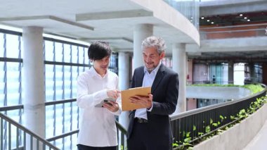 Asyalı son sınıf profesörü, üniversite fakültesi kampüsünde eğitim, akademik ve iş konsepti için yürürken, üniversite öğrencilerine araştırma tezi hakkında danışmanlık yapıyor.