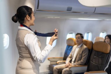 Asyalı uçuş görevlisi, kabin personeli ve havayolu şirketleri için uçağa binmeden önce emniyet kemerini kullanarak güvenlik prosedürünü gösteriyor.