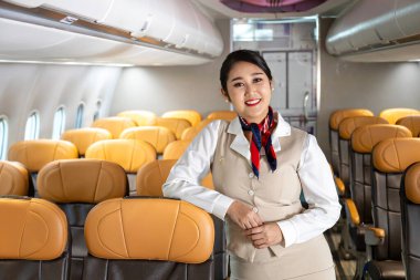 Uçakta gülümseyerek poz veren Asyalı uçuş görevlisi yolcu koltuğuna oturarak yolcu karşıladı.