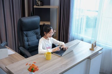 Genç Asyalı liseli kız evde ödevini yapıyor. Eğitim ve eğitim için dizüstü bilgisayarını kullanıyor.