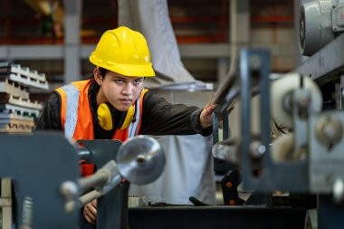 Asyalı sanayi işçisi, güvenlik sanayii inşaatı için çatıdaki metal levha oluşturma makinesinin kurulum değerini kontrol ediyor.