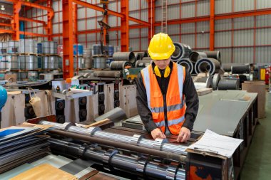 Mühendislik teknisyeni, üretim fabrikasındaki metal levha oluşturma makinesinin çeliğini ölçüyor.