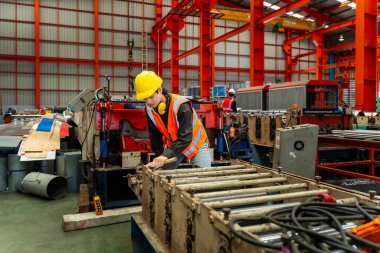 Asyalı sanayi işçisi, güvenlik sanayii inşaatı için çatıdaki metal levha oluşturma makinesinin kurulum değerini kontrol ediyor.