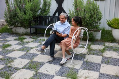 Genç Asyalı anaokulu kızı, öğrenim ve eğitim konsepti için büyükbabasının bahçesinde dijital tablet kullanarak öğreniyor.