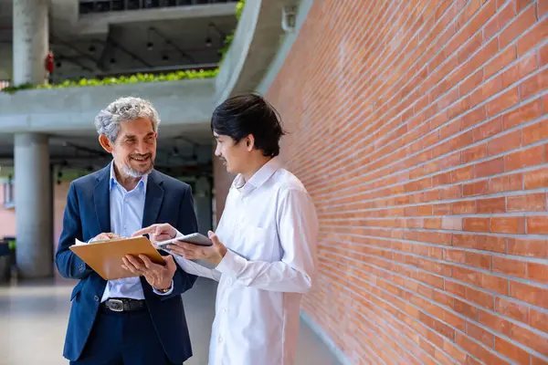 Asyalı son sınıf profesörü, üniversite fakültesi eğitim, akademik ve iş alanında otururken üniversite öğrencisine araştırma tezi hakkında danışmanlık yapıyor.
