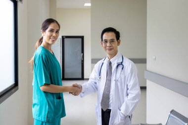 Asyalı doktor ve hemşire ekibi deneyimli uzman hekim konseptiyle tam bakım planı için hastanın tıbbi kayıtları üzerinde çalıştıktan sonra el sıkışıyorlar.