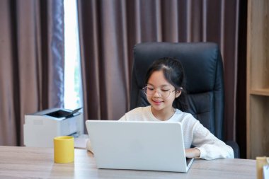 Genç Asyalı liseli kız evde ödevini yapıyor. Eğitim ve eğitim için dizüstü bilgisayarını kullanıyor.