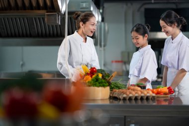 Profesyonel aşçı, genç aşçılık sınıfı öğrencisine restoran mutfağında güzel yemekler ve aşçılık okulu konsepti için taze malzeme hazırlamasını öğretiyor.