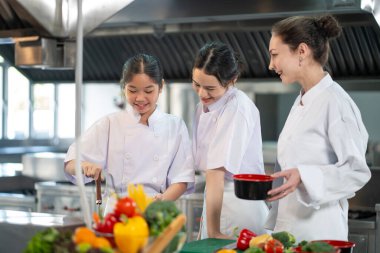 Profesyonel aşçı, genç aşçılık sınıfı öğrencisine restoranın mutfağında güzel yemekler ve aşçılık okulu için taze malzeme hazırlamasını öğretiyor.