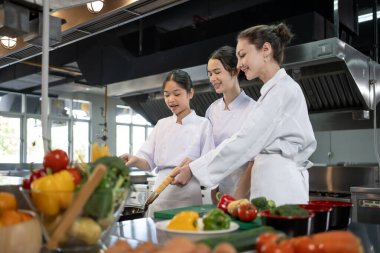 Profesyonel aşçı, genç aşçılık sınıfı öğrencisine restoranın mutfağında güzel yemekler ve aşçılık okulu için taze malzeme hazırlamasını öğretiyor.