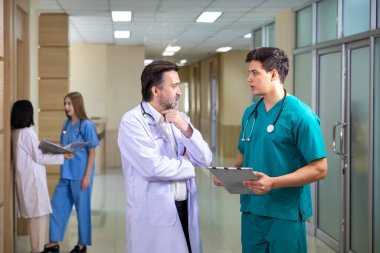 Çeşitlilik doktoru ve hemşire, deneyimli kıdemli hekim uzman doktorla, tam bakım planı üzerine, hastanın tıbbi kayıtlarını tartışıyor ve beyin fırtınası yapıyor.