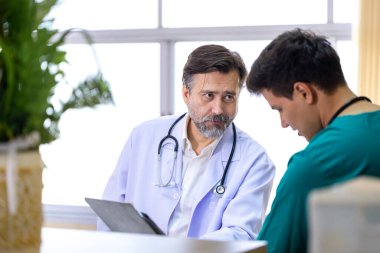 Kıdemli doktor, genç hemşireyle deneyimli bir hekim doktorla kesin bakım planı üzerine hasta kayıtları üzerinde tartışıyor ve beyin fırtınası yapıyor. 