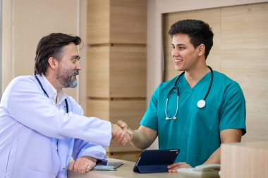 Kıdemli doktor genç hemşireyle tokalaşırken aynı zamanda deneyimli bir hekim doktorla kesin bir tedavi planı için hastanın tıbbi kayıtları üzerine tartışıyordu.