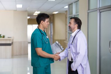 Kıdemli doktor genç hemşireyle tokalaşıyor. Deneyimli hekim doktorla birlikte tam bakım planı için hastanın tıbbi kayıtları üzerine tartışıyorlar.