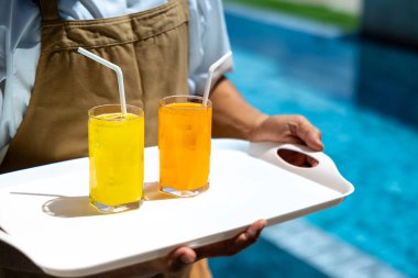Garson yaz boyunca tatil ve seyahat konsepti için lüks oteldeki yüzme havuzunun yanındaki müşteriye iki bardak buzlu tropikal meyve suyu taşıyor.