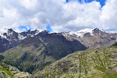 Dağ manzarası, yüksek dağlar, karla kaplı tepeler ve bulutlar.