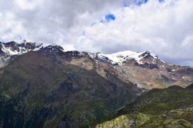 Dağ manzarası, yüksek dağlar, karla kaplı tepeler ve bulutlar.