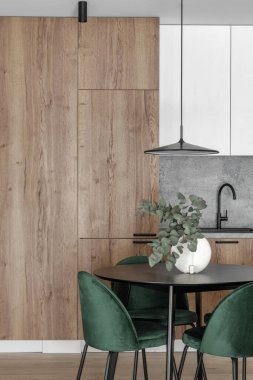 Modern minimalist mutfak ve yemek odası içi ahşap ve beyaz yüzeyler, yeşil sandalyeler ve seramik vazoda okaliptüs. Estetik basit iç tasarım konsepti.