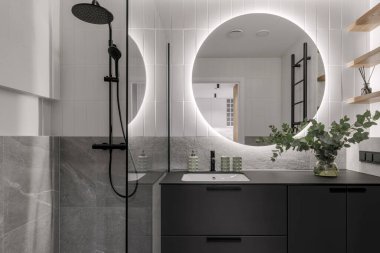 Modern minimalist banyo iç tasarımı gri taş fayanslar, siyah mobilyalar, cam vazoda okaliptüs, yuvarlak ayna. Estetik basit iç tasarım konsepti.