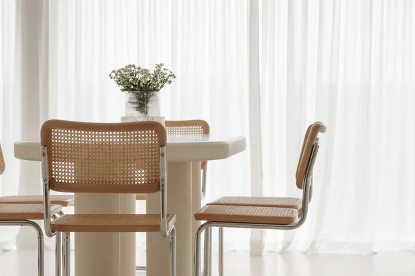 Interior of light dining room with white table, rattan chairs. Japandi interior concept