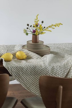 Seramik yemek takımı, keten masa örtüsü, yemek sandalyeleri, limonlar ve yaban bahar çiçekleriyle basit bir yemek masası organizasyonu. Ev dekorasyonu kavramı