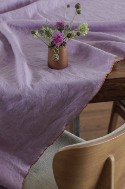Seramik yemek takımları, mor keten masa örtüleri, yemek sandalyeleri, bahar yabani çiçekleri olan basit bir yemek masası organizasyonu. Ev dekorasyonu kavramı