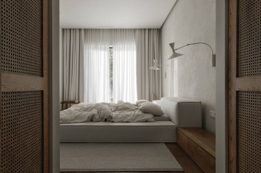 wabi-sabi yatak odası meşe bir komodin, desenli kil duvar dekoru, yumuşak keten çarşaflar, nötr gri bir halı, ve dokuma bir rattan gardırop içerir, doğal malzemeler ve huzur dolu bir karışım yaratır..