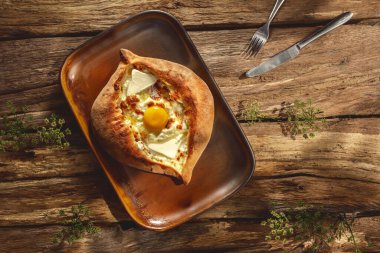 Geleneksel bir Khachapuri otantik bir tabağa dayanır, güneşli bir ışıkta, ahşap bir arka plana yaslanır, altın kabuğunu ve yapışkan peynirini ön plana çıkarır..