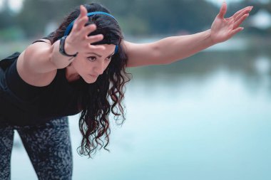 Sportif kadın egzersiz yapıyor, güçlü ve sağlıklı, kollarını esnetiyor, egzersiz için ısınıyor, uzaklara bakıyor. Genç sporcunun silueti vücudunu egzersizlere hazırlıyor..