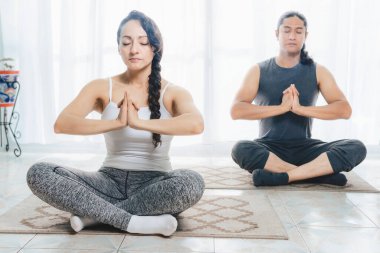 İki orta yaşlı insan içeride yoga yapıyor, pencereden içeri bolca güneş ışığı giriyor, derin meditasyon pozisyonları alıyorlar. Çok fazla sükunet var..