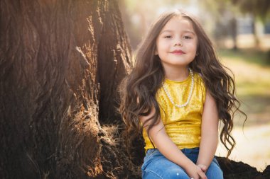 Ağaçta oturan sarışın anaokulu kızı doğada güzel vakit geçiriyor, tatlı bir gülümseme. çocuk günü teması.