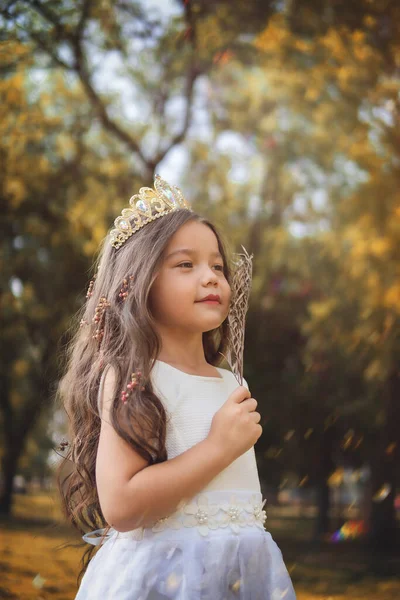 Girl in white dress and princess crown plays in the forest as in a fairy tale, copy space, children\'s day theme.