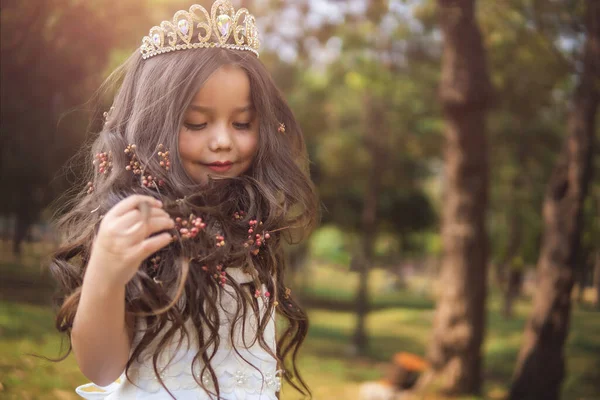 Little girl in white dress and princess crown, she plays with her long blonde hair, copy space, children\'s day theme.