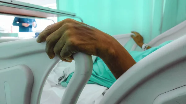 A sick person\'s hand gripping the bed support in a hospital