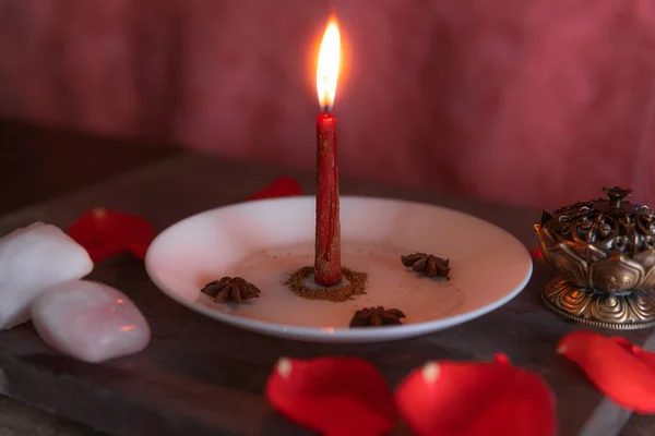 粉红的背景上点燃着一支红色的蜡烛 用肉桂 香和玫瑰石英制成 还有仿制过的糊糊 万圣节 宗教信仰 白色的魔法 图库图片