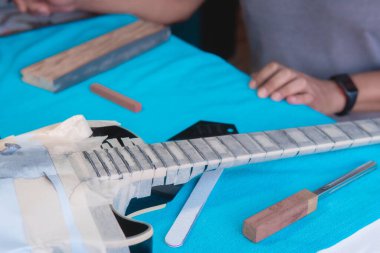 Onarım atölyesindeki siyah elektro gitar tamir eden gitar Luthier, gitar teknisyeni, elektro gitar yakasındaki perdeleri düzenleyici barla hizaladı..