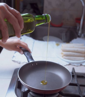 Meksika mutfağında kızgın tavaya yağ dökerken yağ şişesini sadece kadın elleri tutarken görülüyor..