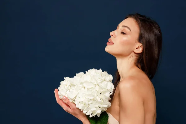 A beautiful fragile girl with long hair holds a bouquet of white flowers in her hands. The concept of lightness or femininity.