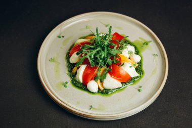 Tabakta bir tabak var. İçinde yeşil, domates ve yumurta dilimleri olan bir salata var..