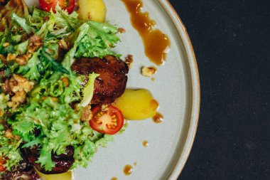 Restoranın siyah masasında patates içeren bir salata var. Tabakta biraz kızarmış lezzetli et, patates, domates ve biraz da yeşil et görebiliyoruz..