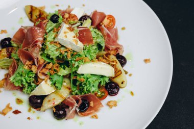 Yeni balık tabağı restoranın müşterilerine servis edilir. Beyaz kasede ve siyah masada. Biraz yeşil et ve balık, peynir ve zeytin var. Harika ve mükemmel görünüyor..